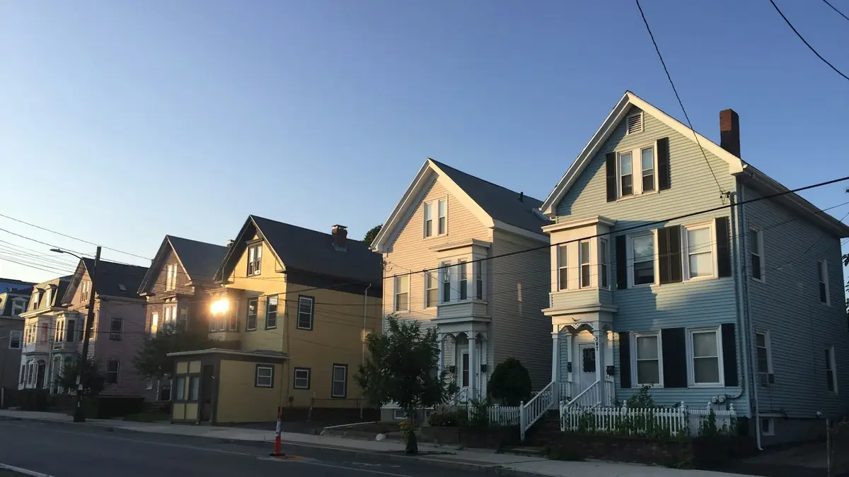 A row of two- and three-story wood-frame multi-family houses on a sunny street - Leak Detection in Revere